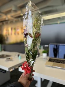 
A hand is holding a bouquet of flowers wrapped in clear plastic, secured with a red ribbon.