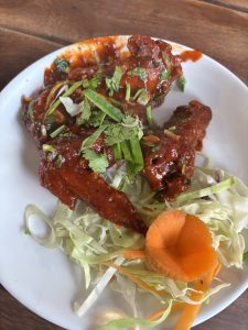 A white plate holds several pieces of chicken wings coated in a rich, red sauce, garnished with chopped green onions and fresh cilantro. 