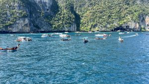 A high-angle view of a large white passenger ferry anchored in the middle of a clear blue tropical bay surrounded by distant green hills.