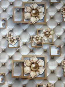 A 3D-style decorative wall panel featuring a quilted silver background with gold studs and large metallic gold flowers emerging from floating square frames. The design has a luxurious aesthetic, with pearl-like centers on the flowers.
