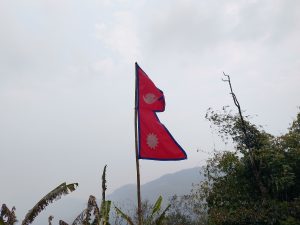 A vibrant red flag features two white sun and moon emblems, representing Nepal, set against a cloudy sky. 