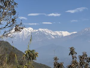 
A panoramic view of snow-capped mountains under a clear blue sky, with scattered white clouds.