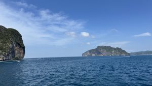 A wide landscape view of massive limestone mountains and islands covered in dense green forest rising from the calm blue sea.