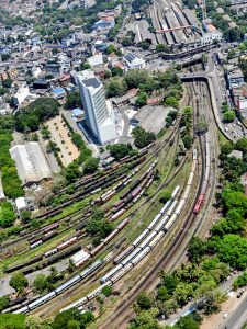 Aerial view of railway tracks and train yards in Colombo, Sri Lanka, captured from the top of the Lotus Tower, showing multiple trains, curved rail lines, surrounding buildings, and nearby roads.
