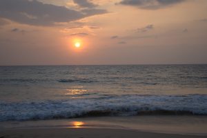 A warm sunset glows over gentle waves rolling onto a quiet sandy beach.
