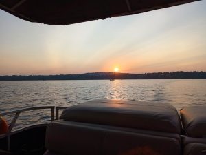 Sunset over Lake Victoria viewed from a speedboat, with warm orange light over the water and a distant forested shoreline.