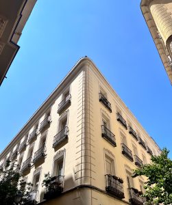 Low-angle view of a classic beige corner building with black wrought-iron balconies against a clear blue sky