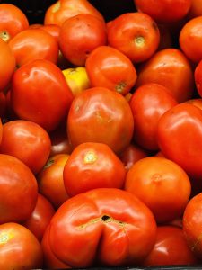 
A close-up image of a variety of ripe red tomatoes piled together with some having slight imperfections.
