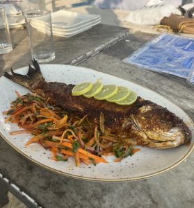 A large fish served on a plate, accompanied by a colorful assortment of fresh vegetables.