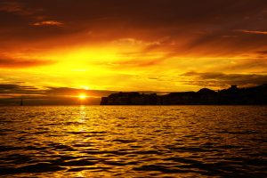 The sun is setting over the sea, painting the sky in bright orange and yellow colors. 