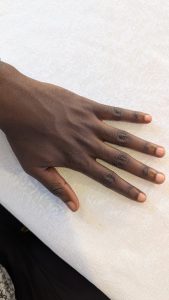 A close-up of a relaxed dark-skinned hand with slightly spread fingers resting on a white textured tablecloth, with trimmed natural nails and a hint of black fabric visible beneath the surface.