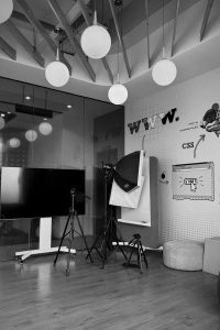 Minimalist workspace with a large screen, tripods, web design graphics, and pendant lights.