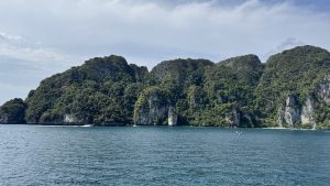 A scenic tropical coastline featuring rugged limestone cliffs densely covered in green jungle foliage bordering the turquoise sea.