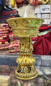 A decorative golden stand with intricate engravings, featuring a bowl-shaped top where a small white candle is positioned.