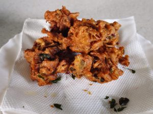 Freshly fried crispy onion pakodas are placed on a paper towel to remove excess oil. This popular South Indian tea-time snack shows rich texture and color, photographed in Kozhikode, Kerala, India.