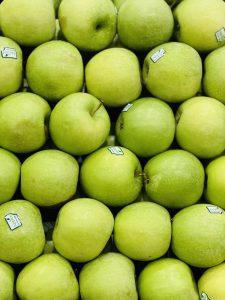 A close-up arrangement of numerous green apples with visible price stickers, neatly stacked together on a surface.