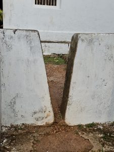 A narrow gap between two white walls leading to a small path, creating depth and perspective in Kozhikode, Kerala. 