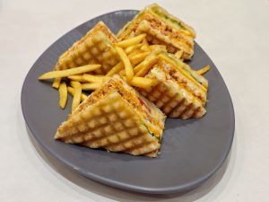 A plate of grilled sandwich triangles served with crispy French fries. The golden toast and colorful filling make the dish look tasty and inviting, photographed in Mavoor Road, Kozhikode. 
