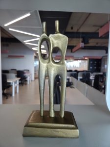 A golden sculpture of two abstract figures facing each other, each with a hollow oval opening in the center.