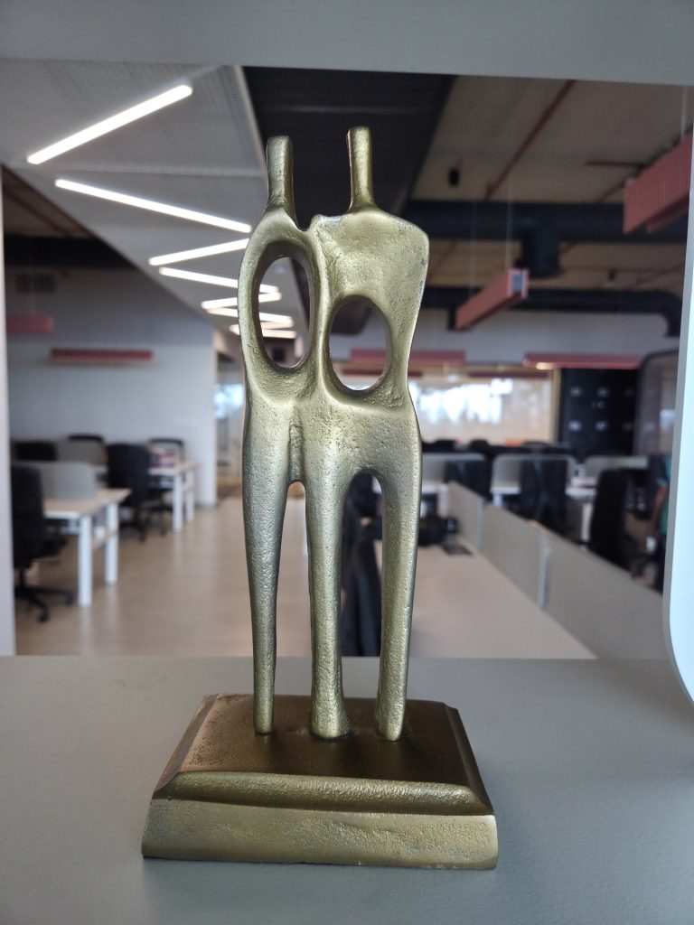 A golden sculpture of two abstract figures facing each other, each with a hollow oval opening in the center.