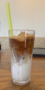 
A clear glass filled with layers of iced coffee and milk, featuring a light green straw.