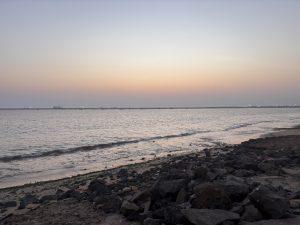 A serene evening coastal scene featuring calm waters reflecting pastel colors of the sunset.