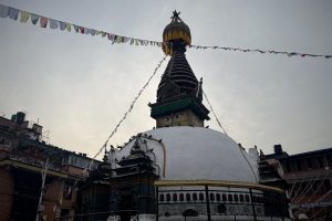 A stupa with a golden spire and prayer flags under a cloudy sky.
