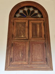 A beautifully crafted wooden window with an arched top and classic panel design. The rich wood texture and simple wall background highlight traditional style in Kozhikode, Kerala.