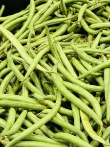 A close-up of fresh green string beans piled together, long and slender with varying shades of green and a slight natural sheen.