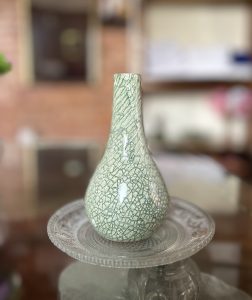 A green ceramic vase with a crackled finish is positioned on a decorative glass plate.