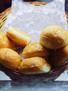 A woven basket filled with several soft, golden-brown bread rolls. 