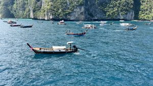 A scenic tropical view of jagged limestone cliffs covered in lush green vegetation rising from clear turquoise ocean water.
