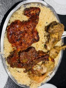 A silver platter filled with fragrant yellow rice topped with several pieces of flavorful grilled chicken. 