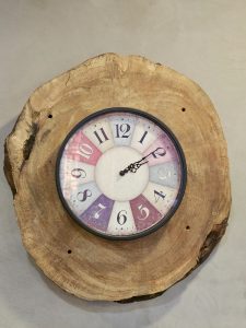 A unique wall clock set on a natural wood slab, combining rustic texture with a colorful dial, was captured indoors in Kozhikode, Kerala.