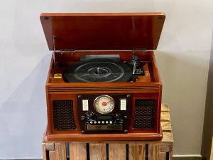 A wooden retro-style music player with its lid open, showing a turntable inside and various dials and buttons on the front for radio and CD functions.