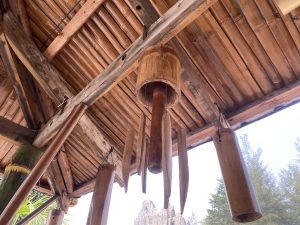 A wooden ceiling structure with beams and a bamboo roof, featuring several bamboo wind chimes hanging from various points.