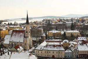 A stunning snowy view of Melk, Austria, featuring a tall Gothic church with a black spire rising above yellow buildings.