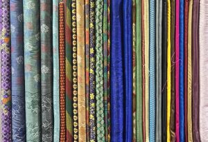A vibrant array of rolled fabrics in various colors and patterns, displayed vertically side by side.