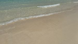 A small wave with white foam rolls onto a clear, shallow sandy beach.
