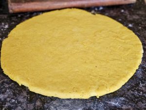 Fresh yellow dough for Wheat Flour Milk Cake rolled flat on a kitchen surface, ready for cooking or baking. The simple preparation scene reflects everyday small-batch baking in Perumanna, Kozhikode. 

