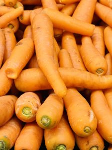 A close-up of a pile of fresh, vibrant orange carrots, showcasing their smooth texture and green tops