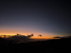 A twilight view over a city valley with an orange horizon fading into deep blue, clouds above mountains, and city lights below.