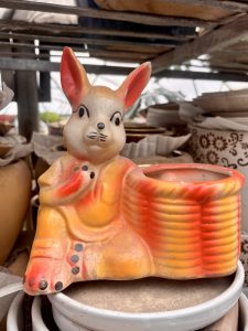 A ceramic rabbit figurine, designed with bright orange and yellow colors, is seated beside a cylindrical planter area