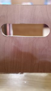 A close up of a brown wooden surface featuring a smooth horizontal cutout handle with a blurred background.
