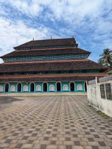 A large, multi-tiered building with a distinctive sloping roof made of tiles, featuring vibrant turquoise walls and arched doorways