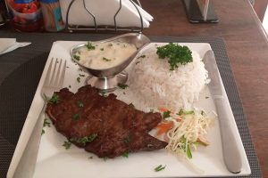 Grilled meat with rice, vegetables, and creamy sauce served on a plate.