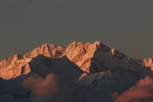 A snow-covered mountain range in Darjeeling glows in the warm light of sunset, showing its rugged peaks.
