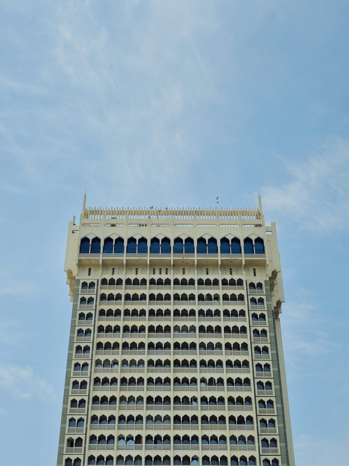 A tall modern building with repeating window patterns in Colaba, Mumbai. The simple symmetry and clean blue sky create a neat and minimal architectural view.