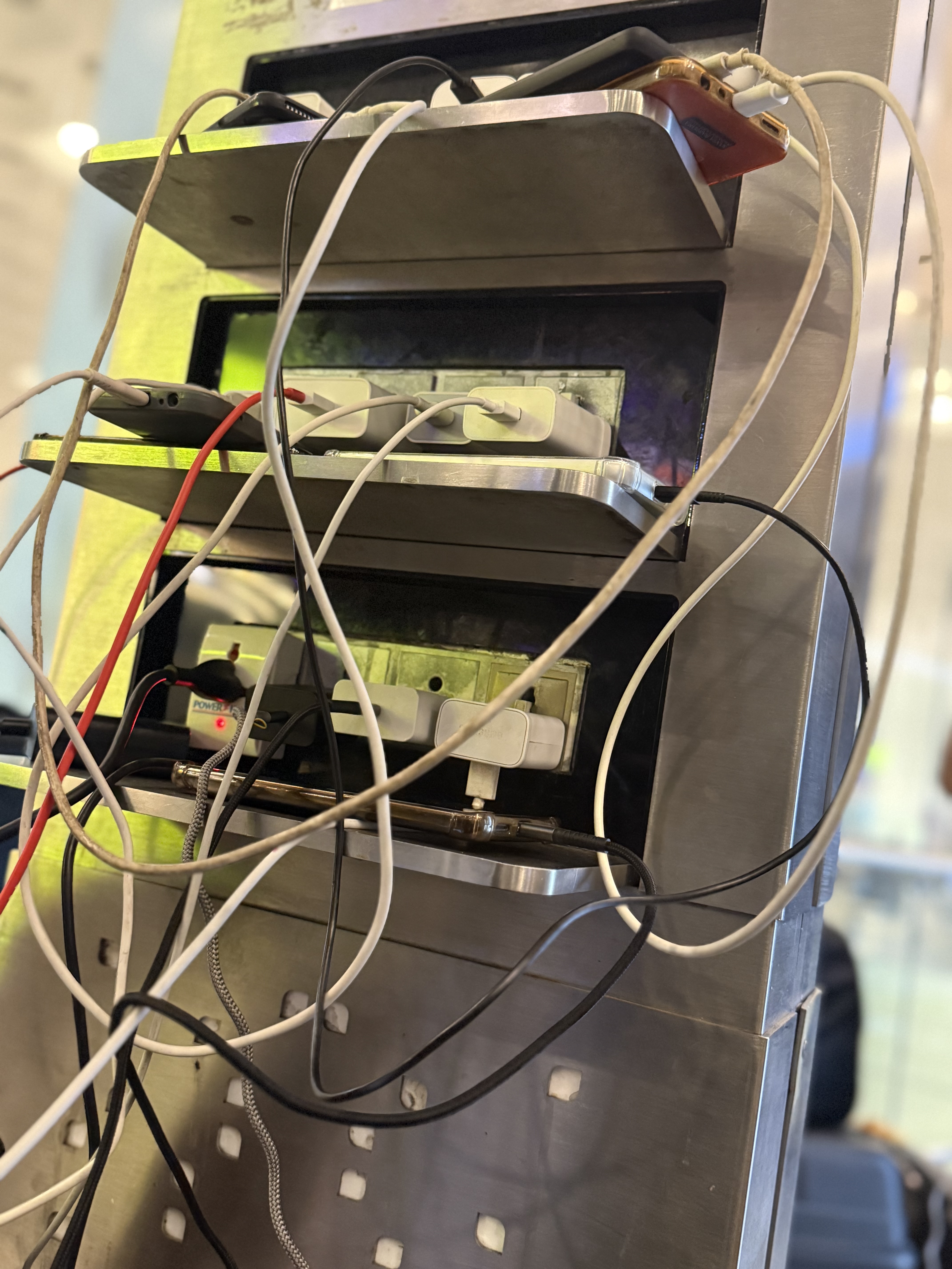 A charging station at the Mumbai Airport. Various charging cables are tangled and connected to devices and power outlets.