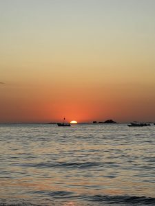 
A serene sunset over a calm ocean with gentle waves, where the sun is partially dipped below the horizon, casting warm orange and yellow hues across the sky.